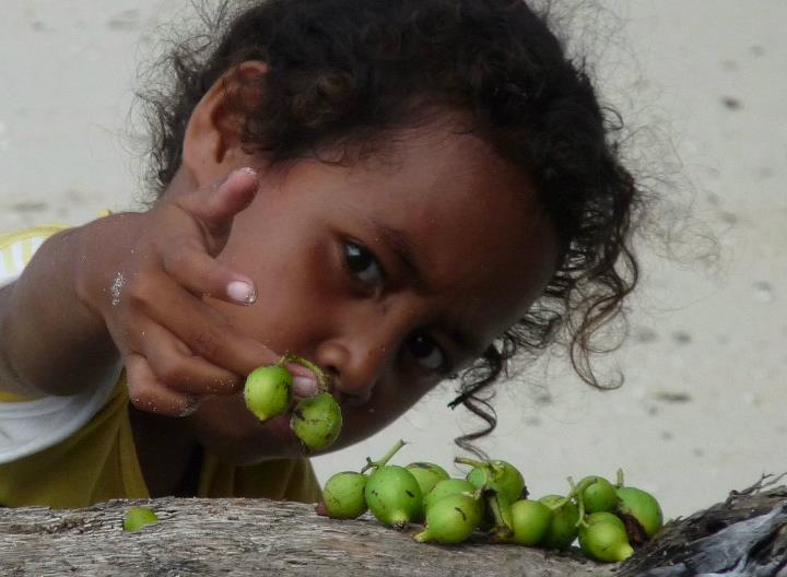 Papuan girl playing with green fruits in Cenderawasih Bay
