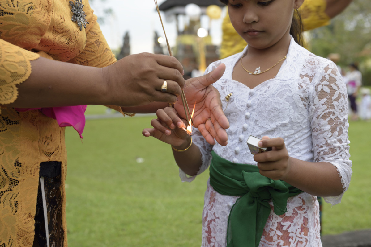 Balinese mother helps her daughter light an incense stick
